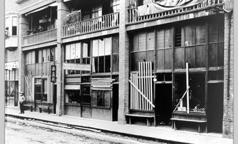 Black and white photo of boarded up buildings.