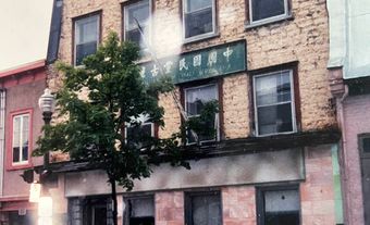 Un bâtiment de trois étages avec une enseigne verte avec des caractères chinois et un arbre devant.