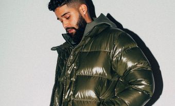South Asian man in a puffer jacket posing by looking downward.