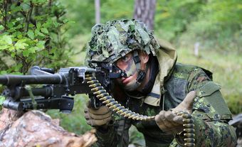 Un soldat canadien vise une mitrailleuse polyvalente C6 tout en tenant une bande de munitions.