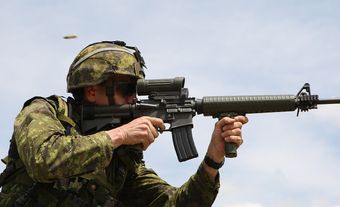 Soldier in CADPAT TW uniform firing a C7A2 rifle with a C79A2 optic and vertical grip.