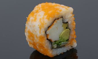 A single sushi roll with the rice with roe outside. Inside the seaweed, there is imitation crab and avocado.