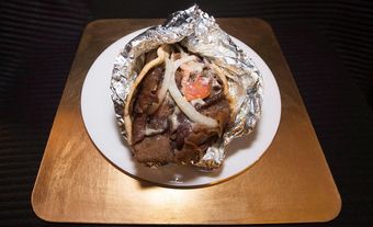 Halifax donair wrap wrapped in aluminium foil on a white plate on a brown table.