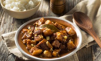 A plate with big meat chunks in a brown liquid, with a bowl of rice on the side.
