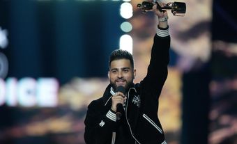 A man in a black jacket holding up an award and a microphone.