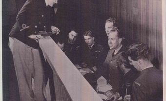 Lieutenant Carol Hendry (standing) and comrades shown plotting positions on tactical table during a tactical game, 1944. Slacks were only worn on the job due to the the amount of time spent on the floor.