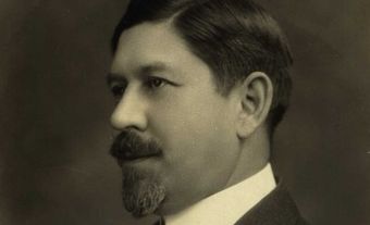A monochromatic picture of a man in a suit with short hair, a beard, and a mustache.