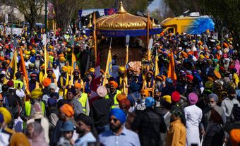 Une foule de personnes défilant à côté d'un char de parade. Certaines personnes portent des drapeaux jaune et orange.