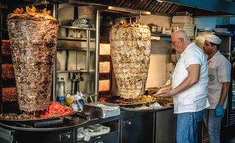 Two batches of shawarma in a kitchen with two cooks