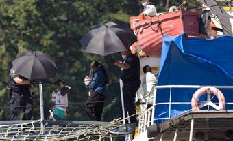 South Asian people escorted off a ship by two CBSA agents holding black umbrellas.