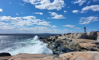 Rochers de granite le long d’un rivage avec un phare au loin.